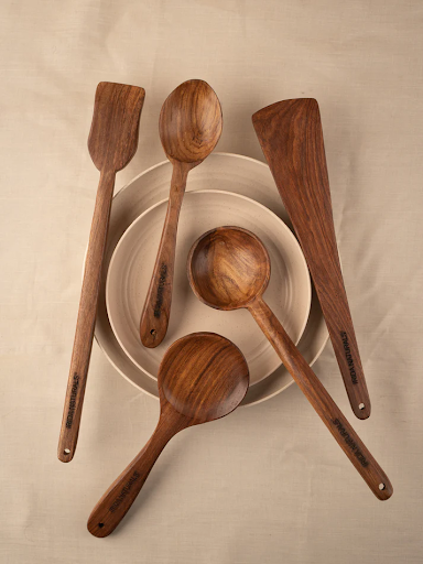 A set of five wooden ladle on stacked ceramic plates against a beige cloth background.